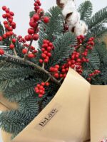 Kompozycja świąteczna z gałązkami ilexu i świerku w złotym papierze